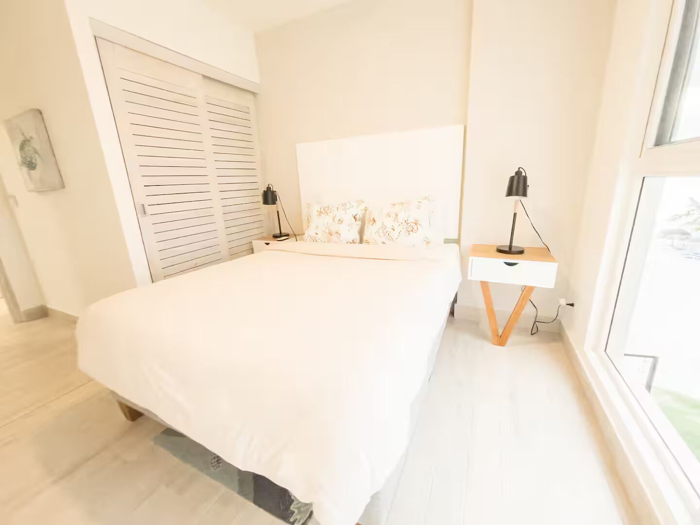 A bedroom with a bed, a bedside table with a lamp, a wardrobe, and a window.
