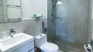 Casa de banho moderna com lavatório branco, sanita e cabine de duche em vidro.