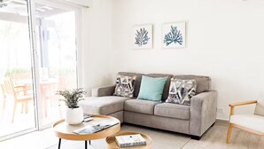A modern living room with a grey sectional sofa, two round wooden coffee tables, and a white armchair. There are two framed artworks on the wall and a potted plant on the coffee table. - Seashore Villa Retreat -C6-PBA- 2 bed, 2 bath (Punta Chame)