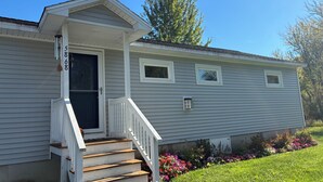 A single-story house with a front porch, a staircase, and a small garden with colorful flowers. - Lakefront 2-bedroom home with dock and AC, minutes from Chautauqua, Sleeps 6 (Mayville)