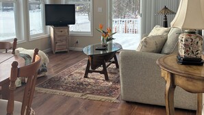 A living room with a television, a sofa, a coffee table, and a dining area with chairs. - Lakefront 2-bedroom home with dock and AC, minutes from Chautauqua, Sleeps 6 (Mayville)