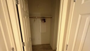 En smal hall med vita dörrar på båda sidor, trägolv och en liten hylla med några få föremål på väggen.