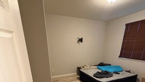 Ett sovrum med en säng, en väggmonterad lampa och ett fönster med persienner.