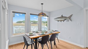 A dining area with a view of a dock and water, a large fish decoration on the wall, and a stained glass pendant light. - Remodeled Center Island Home, Marsh Views, 2 Golf Carts, Stellar Sunsets (Fripp Island)