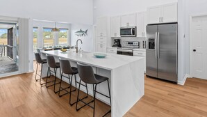 A modern kitchen with a large island, bar stools, stainless steel appliances, and a view of the outdoors. - Remodeled Center Island Home, Marsh Views, 2 Golf Carts, Stellar Sunsets (Fripp Island)