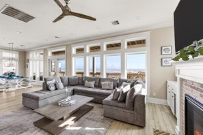 A spacious living room with a large sectional sofa, a fireplace, and a view of the ocean. - Beachfront Home- Hot Tub & Private Walkover (Galveston)