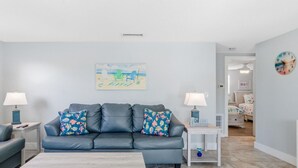 Uma sala de estar moderna com um sofá de couro cinza, duas poltronas combinando, uma mesa de centro de madeira e uma pintura de uma cena de praia na parede.