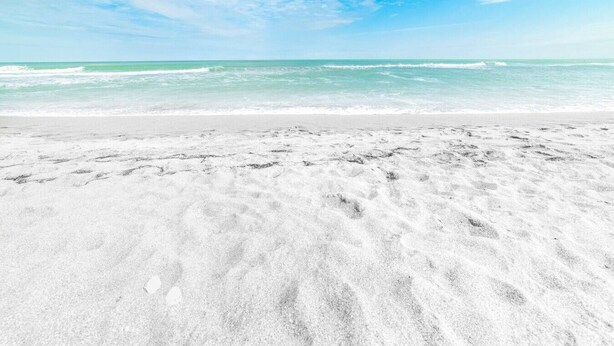 Uma praia com pegadas na areia e céu azul límpido.