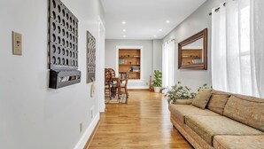 Una sala moderna con suelo de madera, un sofá, una zona de comedor con sillas y una mesa, y una estantería.