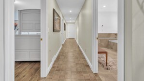 Un pasillo con piso de madera, paredes blancas y una puerta que da a un baño.
