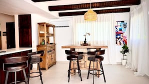 A modern kitchen with a central island, bar stools, wooden cabinets, and a hanging light fixture. - Villa Postosomar Cabarete (Cabarete)