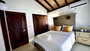A bedroom with a wooden ceiling, a bed with a white quilt, a nightstand, and a wooden door. - Villa Postosomar Cabarete (Cabarete)