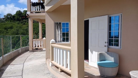 A balcony with a white chair and a door, surrounded by a beige wall and a fenced area.