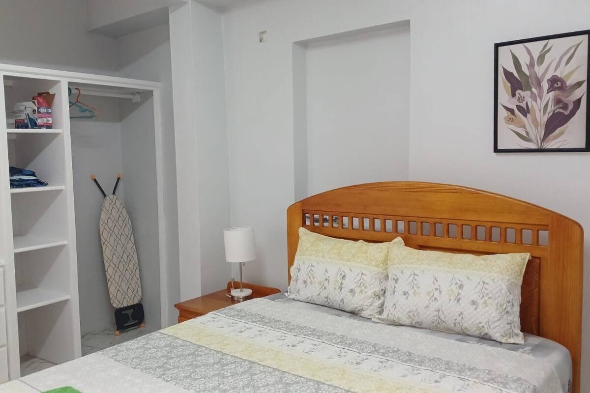 Un dormitorio con una cama de madera, un armario blanco y una mesita de noche con lámpara.