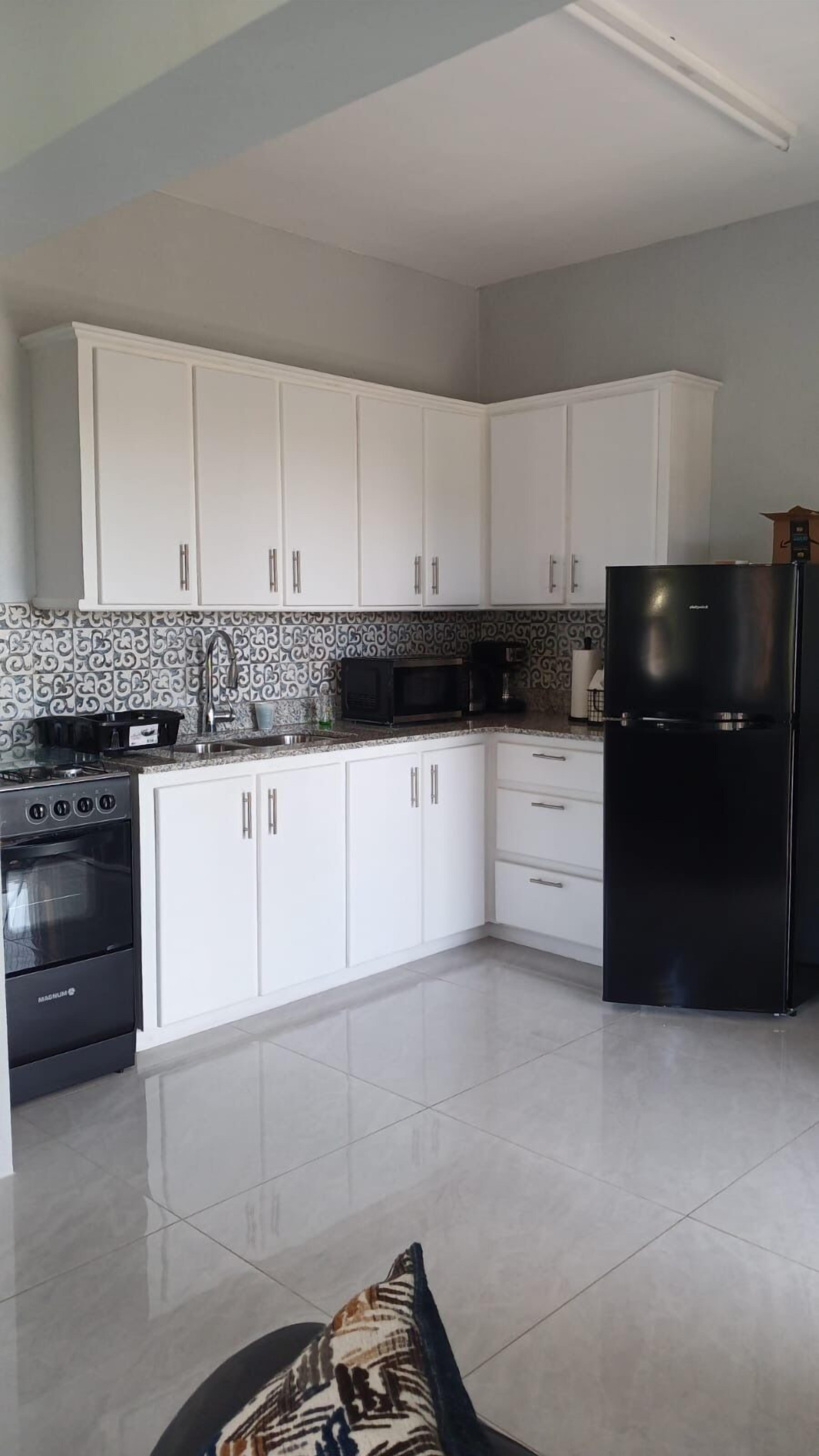 A modern kitchen with white cabinets, a black refrigerator, and a microwave.