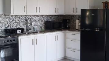 A modern kitchen with white cabinets, a black refrigerator, and a microwave.