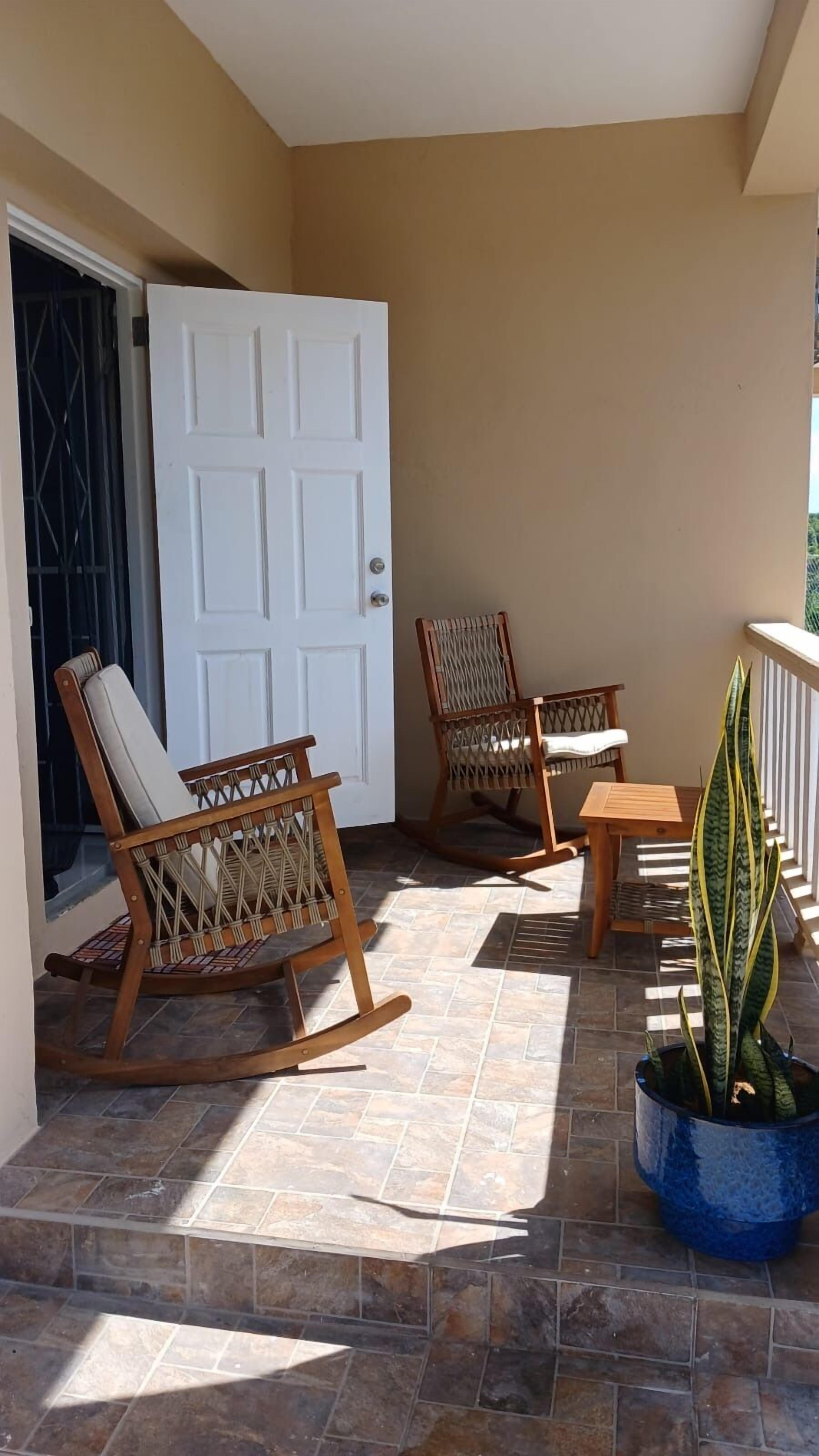 A balcony with two rocking chairs, a small table, and a potted plant.