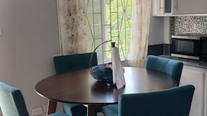 Un comedor con una mesa redonda, seis sillas color turquesa y una ventana con cortinas.