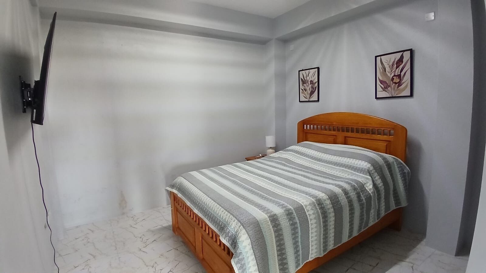 A bedroom with a wooden bed, a wall-mounted TV, and two framed floral pictures.