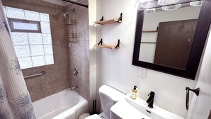 A bathroom with a bathtub, toilet, and sink. There is a window with a view of the outside, and a mirror above the sink. - Cozy 3-bedroom house in Granger, Indiana (Granger)