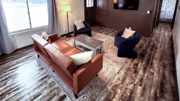 A living room with a brown leather sofa, a dark blue armchair, a wooden coffee table, and a floor lamp. - Cozy 3-bedroom house in Granger, Indiana (Granger)