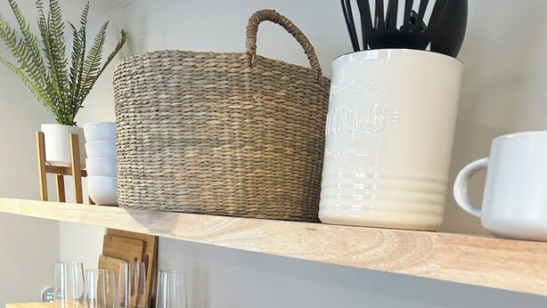 Una cocina con estantes de madera, un microondas, una tetera y un bloque de cuchillos.