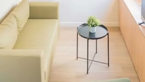 Un salon moderne avec un canapé, une petite table ronde ornée d’une plante et un téléviseur posé sur un meuble en bois.