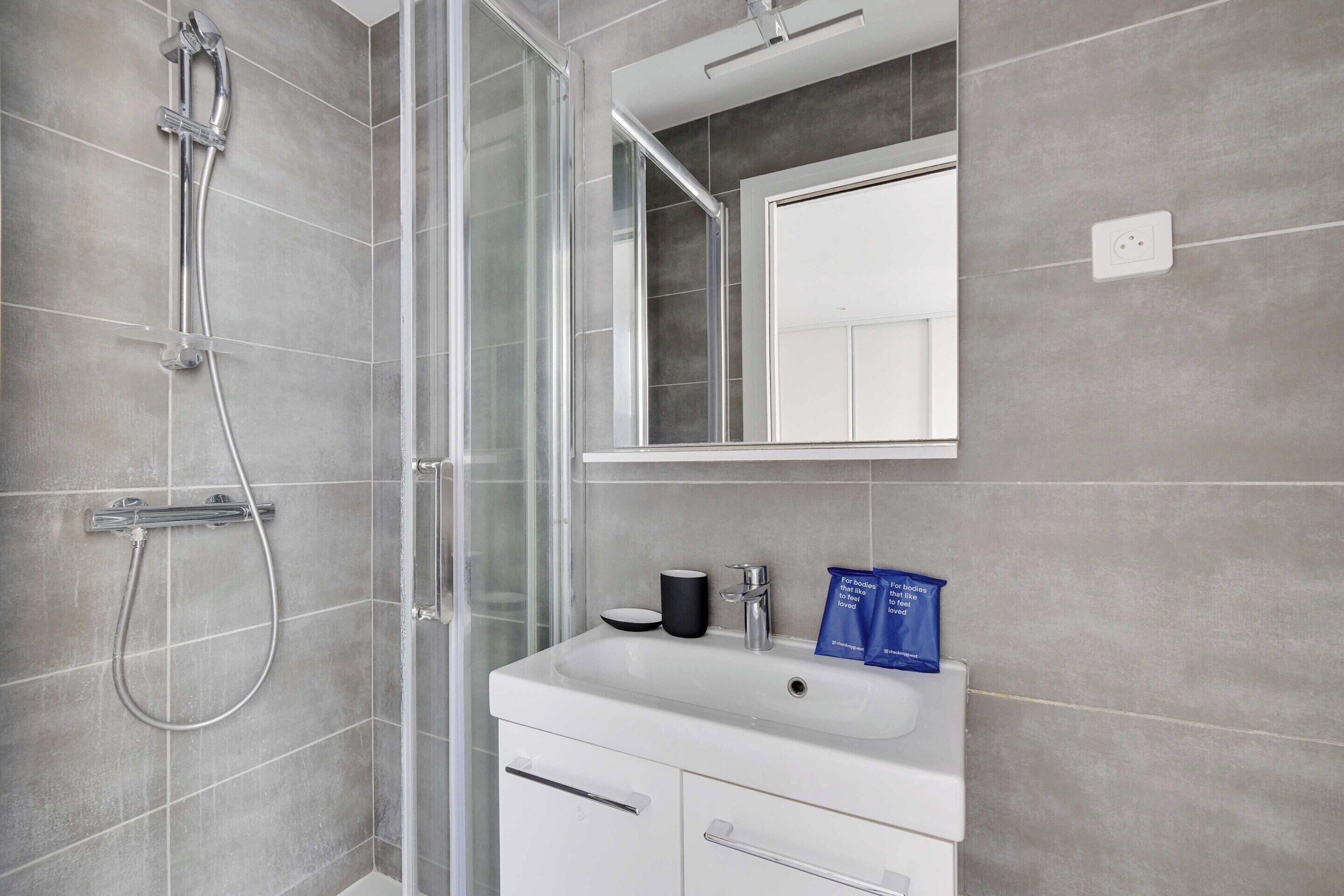 A modern bathroom with a glass shower enclosure, a white sink, and a mirror above it.