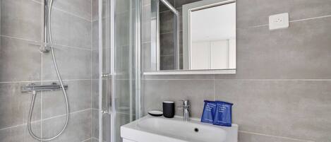 A modern bathroom with a glass shower enclosure, a white sink, and a mirror above it.
