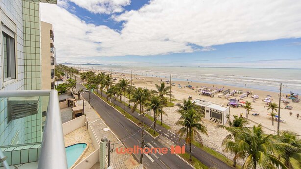 A beach view from a balcony with palm trees and a pool. - Apartamento na Praia Grande com Acesso a Praia (Praia Grande)