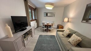 Ein Wohnzimmer mit Fernseher, einer Couch, einem Esstisch und einem Teppich.