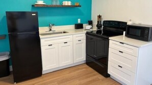 Une cuisine de taille réduite avec des meubles blancs, un réfrigérateur noir, un four à micro-ondes et une cuisinière.