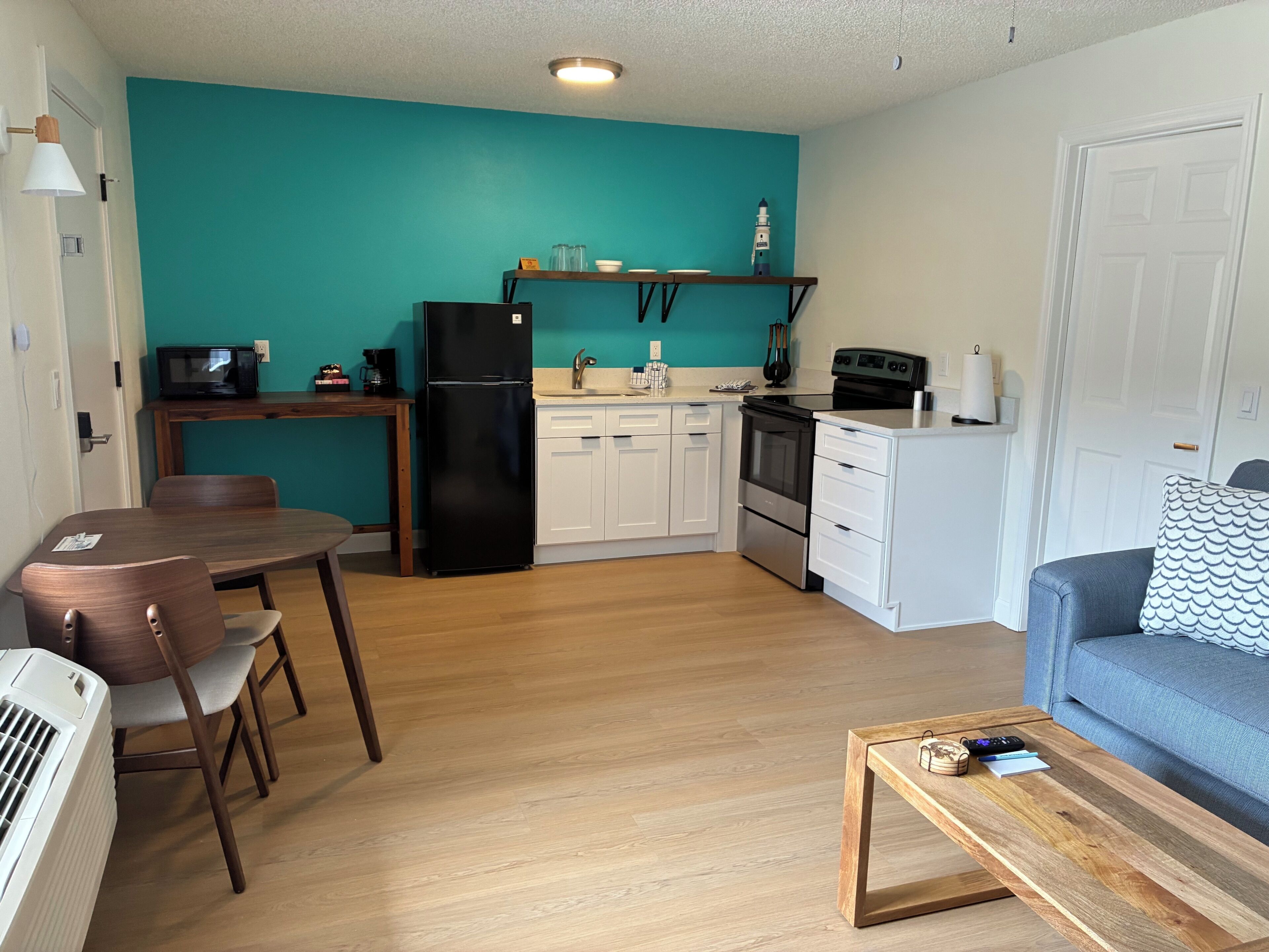 A compact kitchen with a refrigerator, stove, microwave, and a small dining area with chairs and a table.