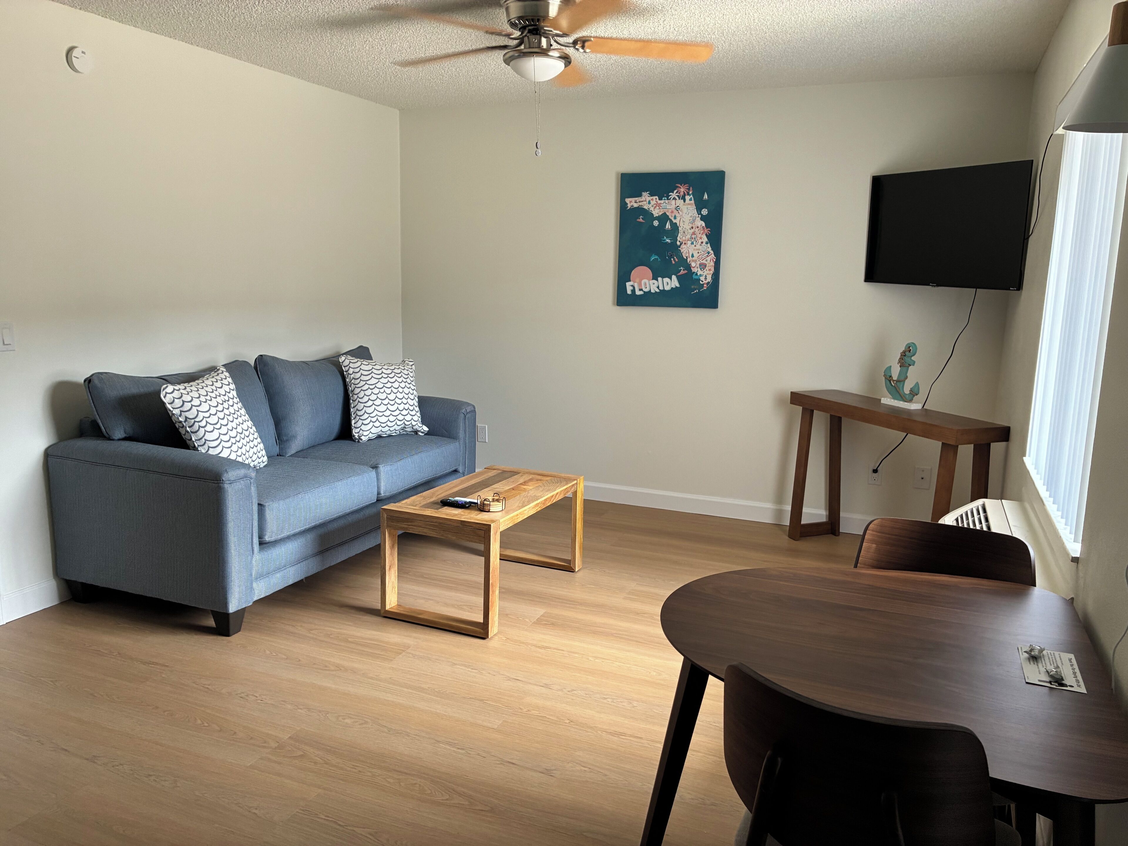 Una sala de estar con sofá, mesa de centro, mesa de comedor y ventilador de techo.