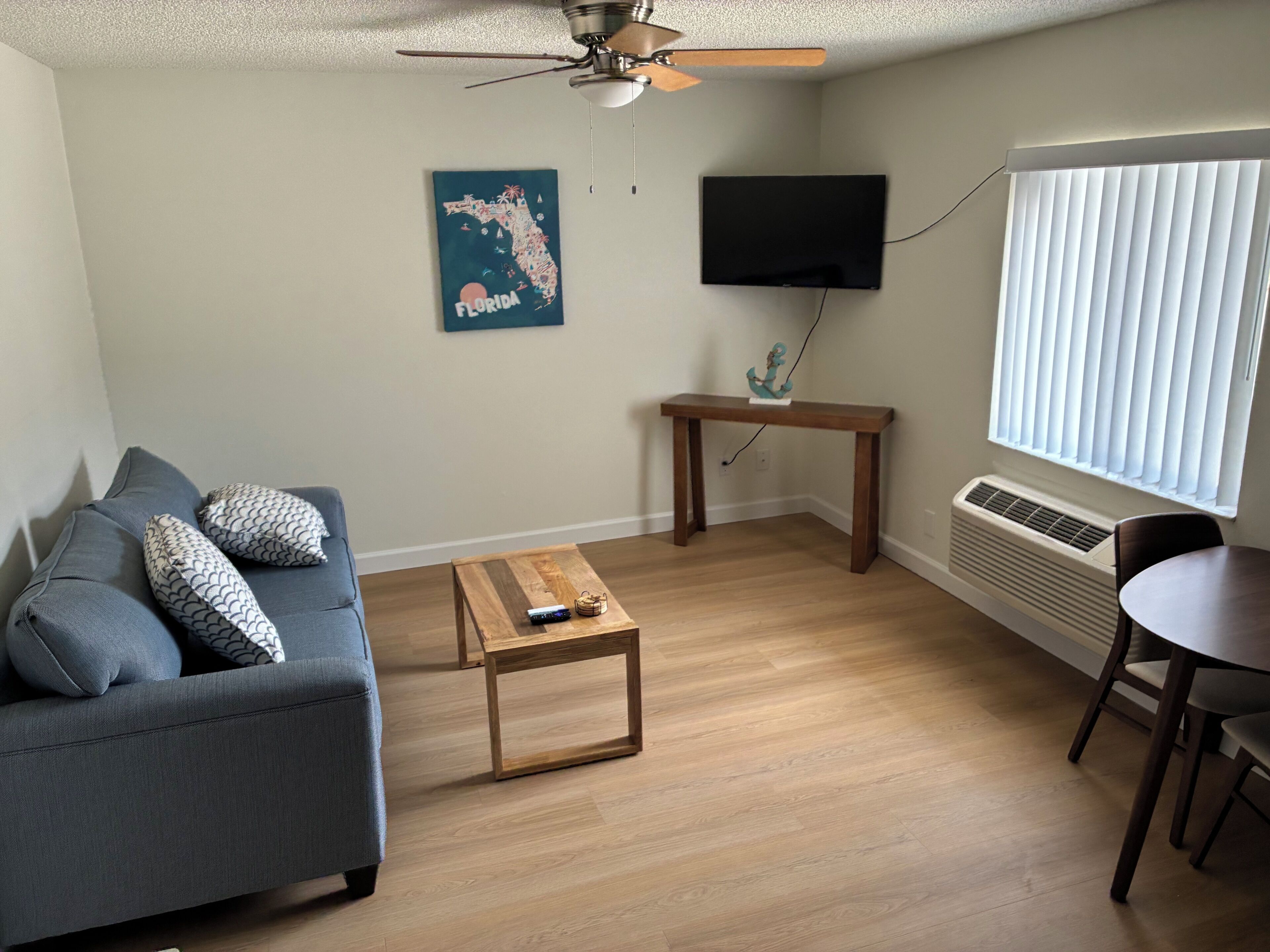 A living room with a sofa, coffee table, TV, and a window with blinds.