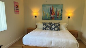 Une chambre à coucher avec un lit en bois, deux tables de chevet, une commode, un tableau au mur et deux lampes fixées au mur.
