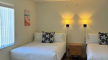 Une chambre avec deux lits, un ventilateur de plafond, des lampes de chevet et une fenêtre avec des stores.
