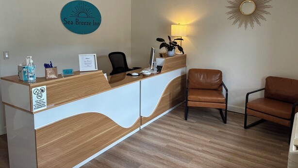 Un comptoir d’accueil avec une enseigne indiquant « Sea Breeze Inn », un ventilateur de plafond, une lampe fixée au mur et deux chaises.