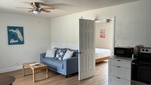 Un espace de vie compact comprenant un canapé, une petite table, un lit, un four à micro-ondes et une cuisinière.
