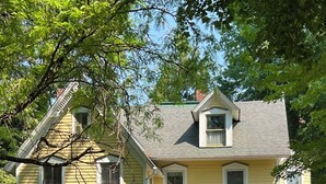 A two-story yellow house with a front porch, a chimney, and a small balcony. - Historic Kugler Cottage, built 1871, Charming 5-Bedroom Stay (Oil City)
