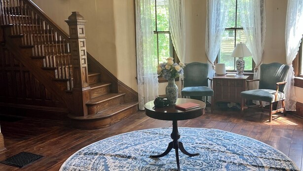 A spacious room with a large wooden staircase, a round table with a blue patterned rug, and a chandelier. - Historic Kugler Cottage, built 1871, Charming 5-Bedroom Stay (Oil City)