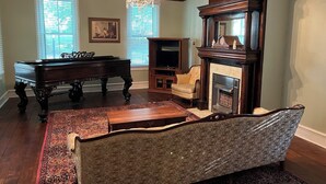 A living room with a grand piano, a sofa, a fireplace, and a chandelier. - Historic Kugler Cottage, built 1871, Charming 5-Bedroom Stay (Oil City)