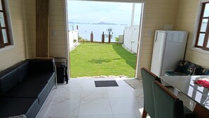 Habitació amb vista a un jardí i una massa d'aigua. Inclou un sofà, una taula i un frigorífic.
