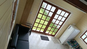 Habitació amb un sofà negre, una taula petita, un frigorífic i una finestra gran amb vista a un camp de gespa verd.