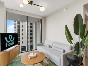 A modern living room with a sofa, a coffee table, and a TV on a wooden console. - 2BR Walk to FIFA Fan Fest | Free Parking (Miami)