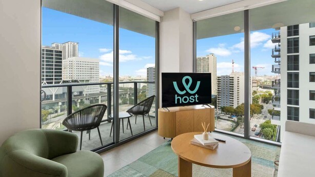 Une chambre d’hôtel moderne avec de grandes fenêtres, un balcon avec des chaises et une vue sur le paysage urbain.