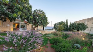 Un jardin avec un mur en pierre, un sentier et un bâtiment doté d’une terrasse.