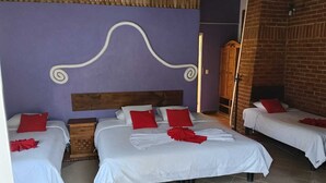 Habitación de hotel con tres camas, cabecera de madera y pared de ladrillo.
