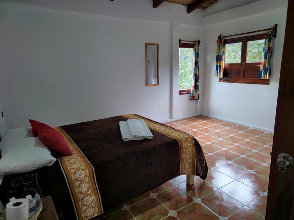 Un dormitorio con cama, ventana con cortinas, espejo y suelo de baldosas.