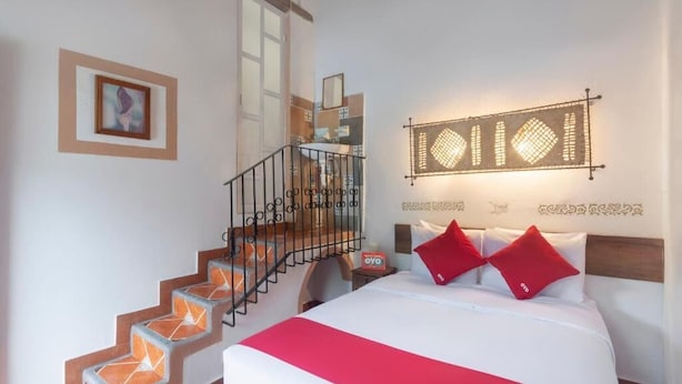 Un dormitorio con cama, almohadas rojas, una escalera y una lámpara fijada a la pared.